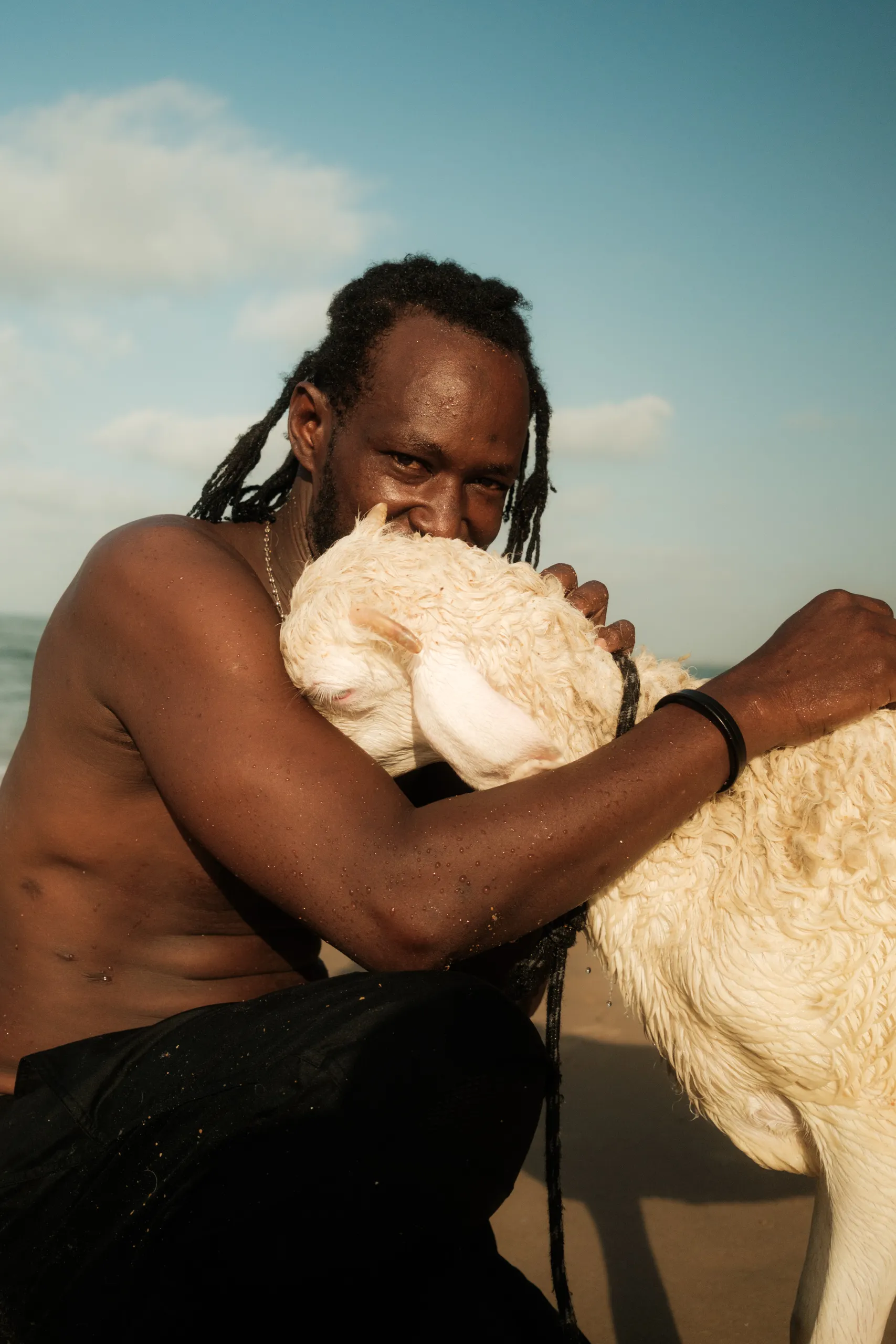 A man holding his sheep on the beach