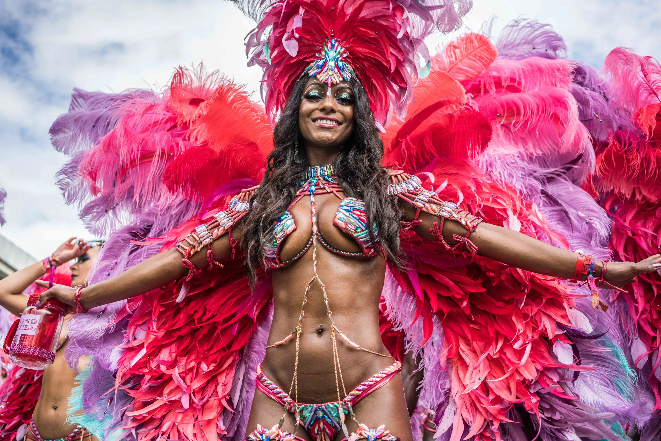 A masquerader in pink feathers with her arms outstretched
