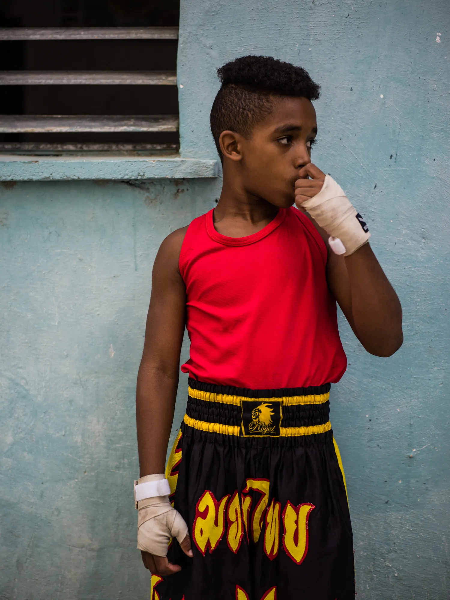 A young boxer in a red vest against a turquoise wall
