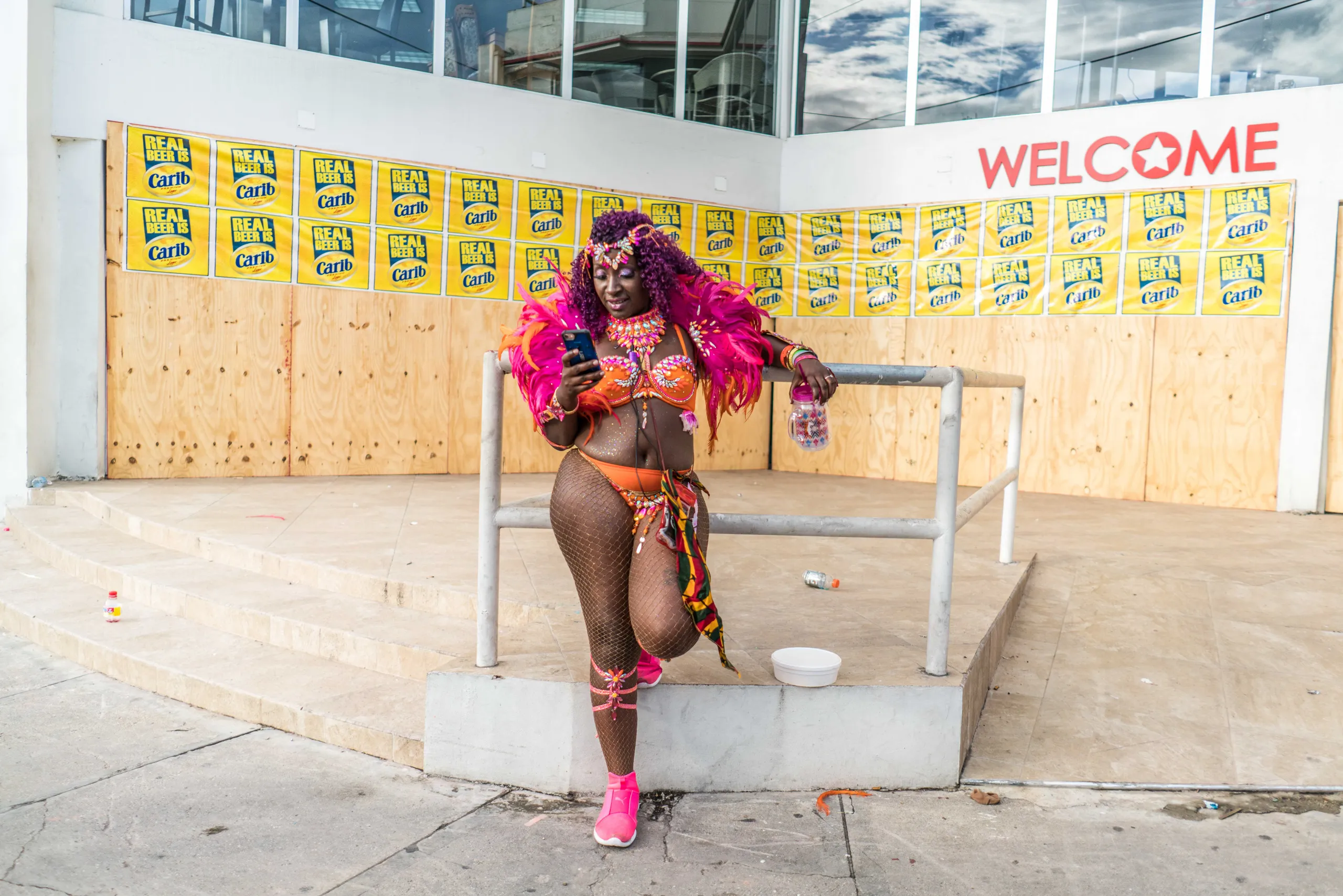 A masquerader in pink beside a yellow welcome wall